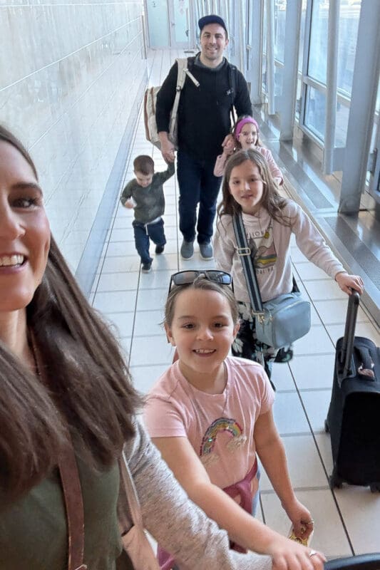 Family walking through airport with luggage after surprising kids with a Disney trip and heading to Florida