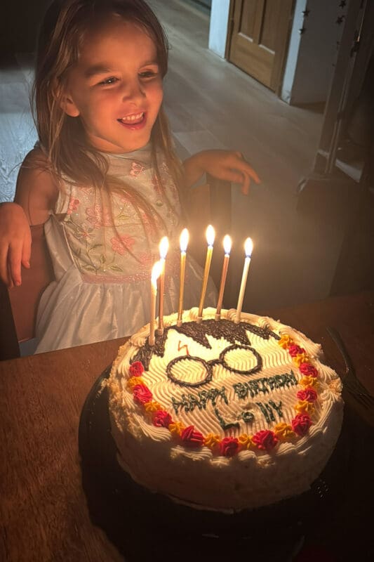 young girl smiling at harry potter birthday cake with candles lit and glasses design