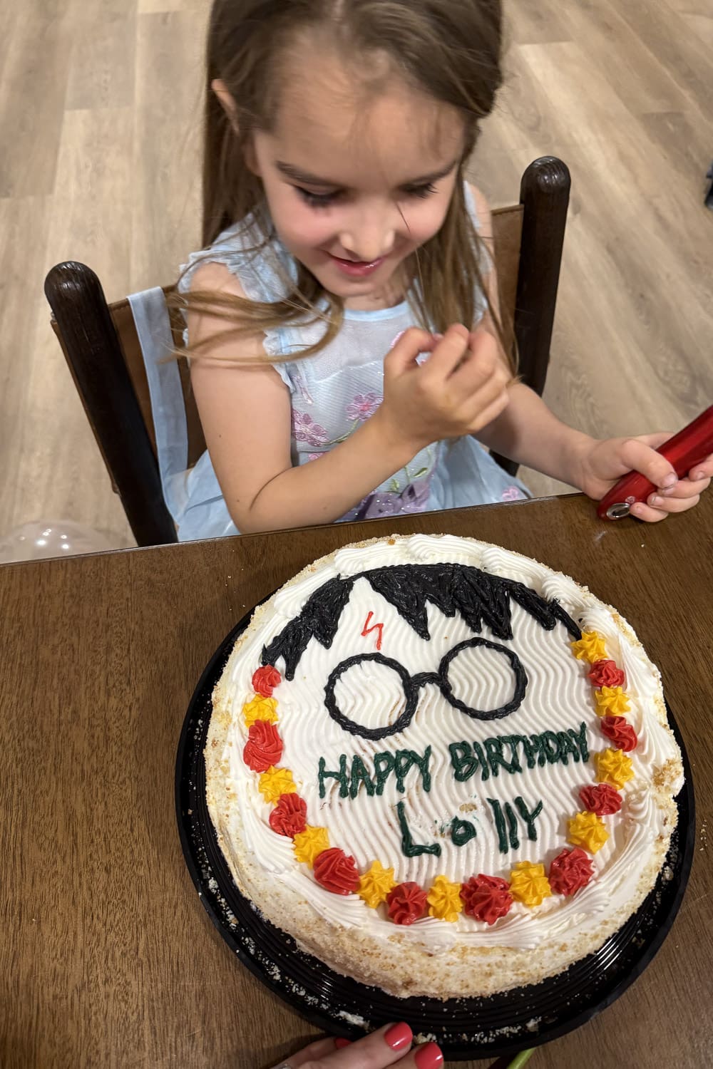 young girl smiling at harry potter cake with glasses design while holding lighter at birthday table