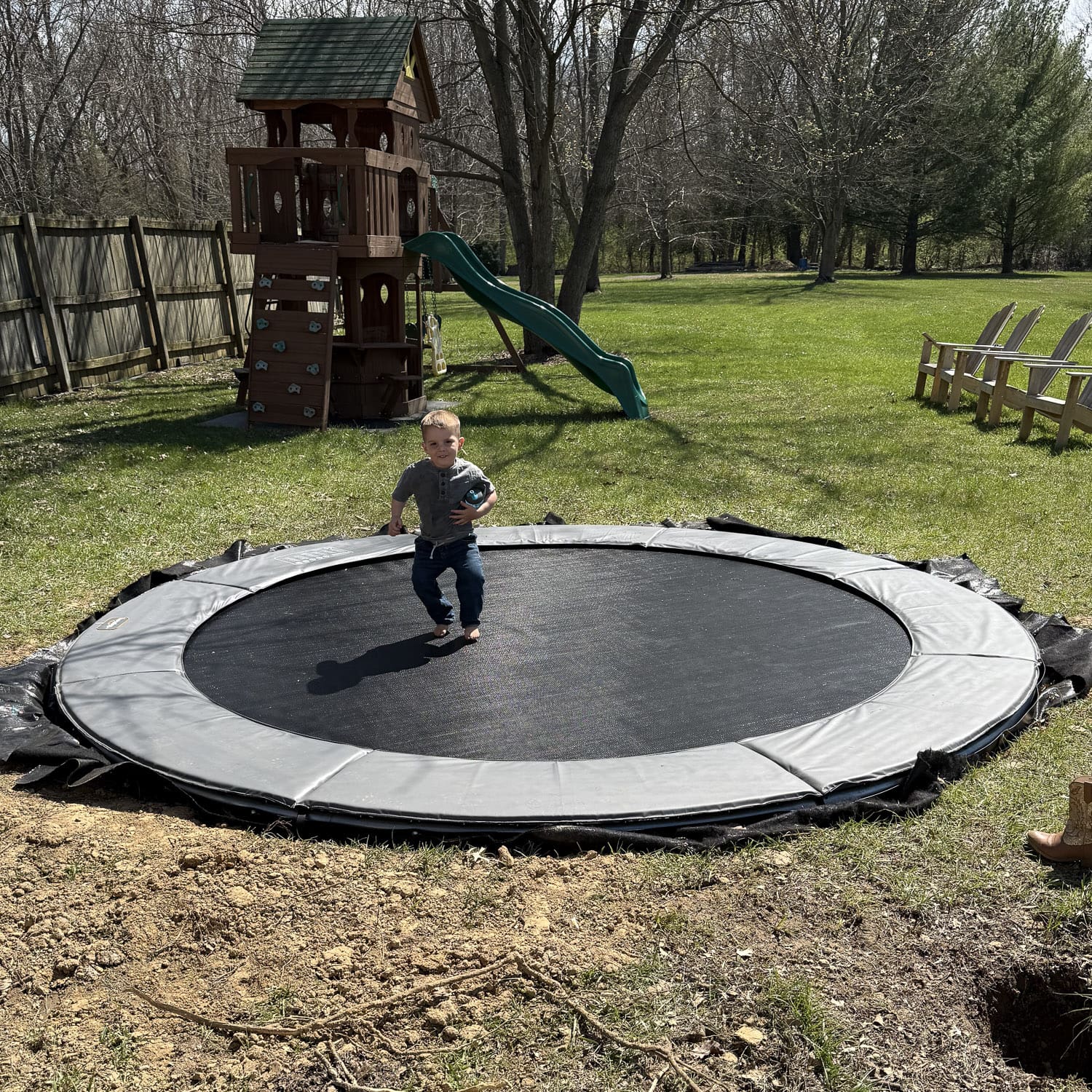 DIY in-ground trampoline installation in progress with child standing on trampoline and freshly dug soil around the pit