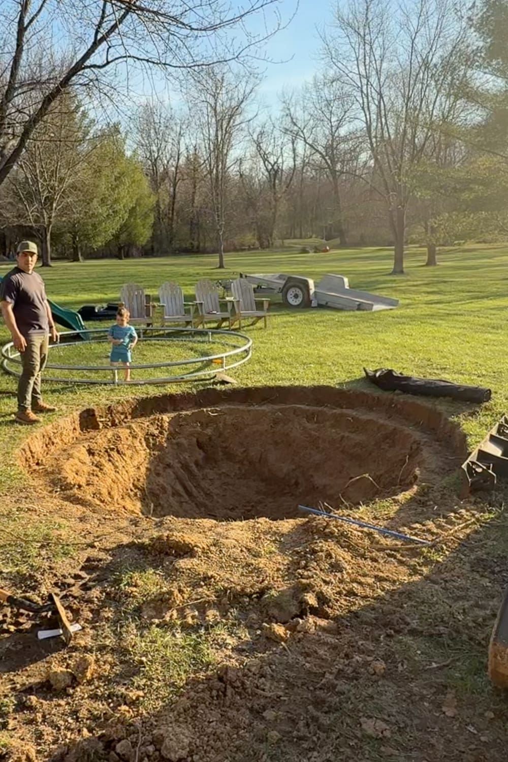 Large in-ground trampoline pit fully dug in backyard with sloped sides and trampoline frame nearby for installation