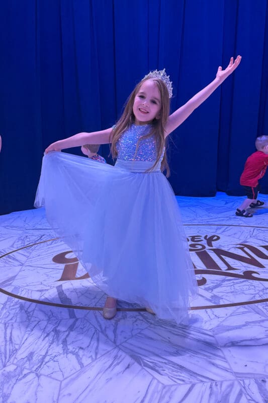 little girl in blue princess dress and tiara twirling on disney cruise ship during kids themed event with disney cruise decor