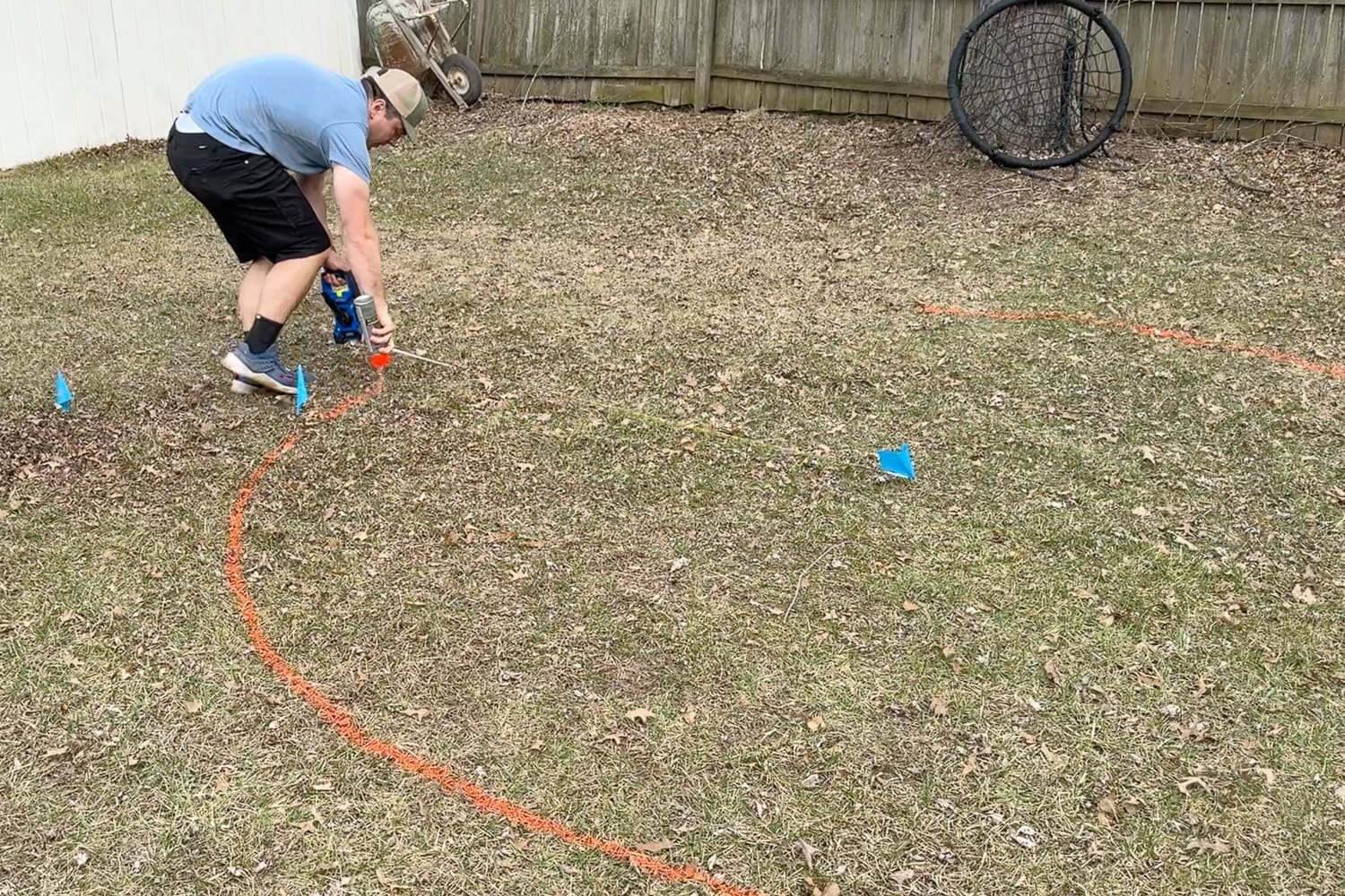 Marking the outline for an in-ground trampoline using spray paint and stakes in a backyard before digging the hole