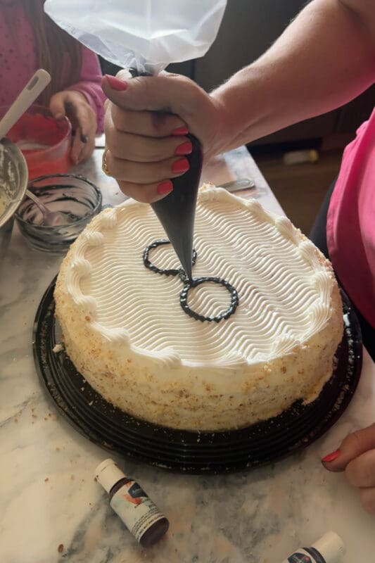 piping black frosting to create harry potter glasses on white birthday cake