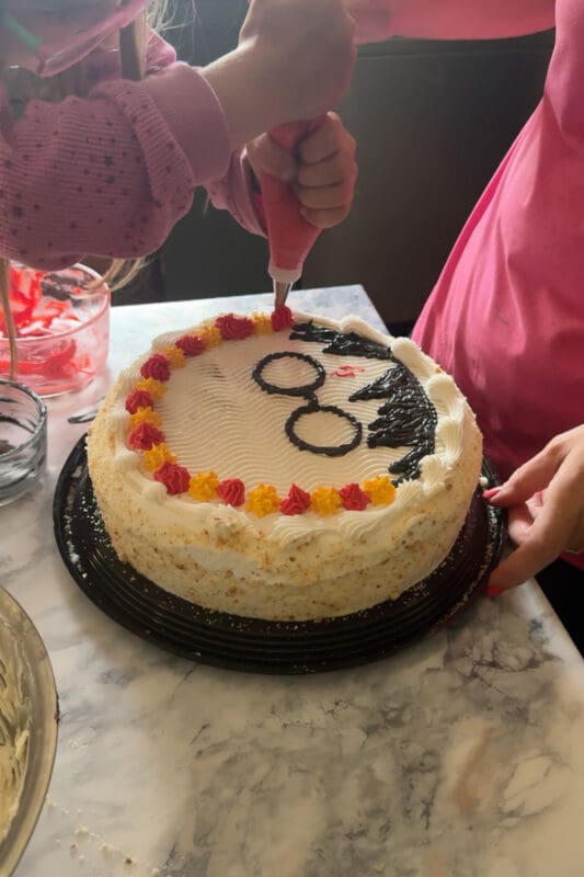 piping red frosting between yellow stars to create colorful border on harry potter cake