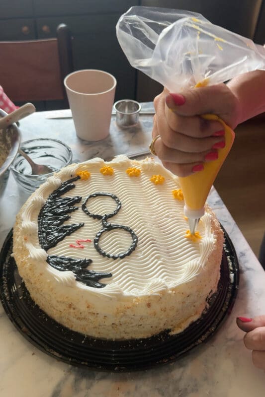 piping yellow star border around homemade birthday cake with glasses and lightning bolt design