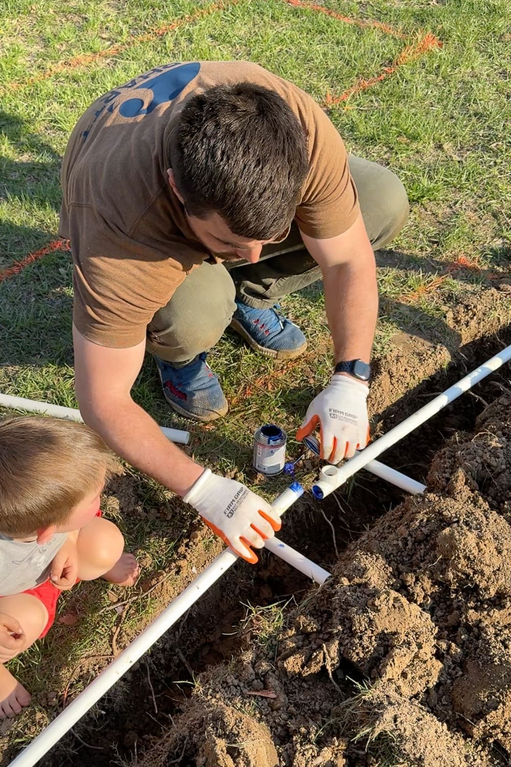 Applying PVC primer and cement to pipe joints before connecting them in a DIY raised bed irrigation system