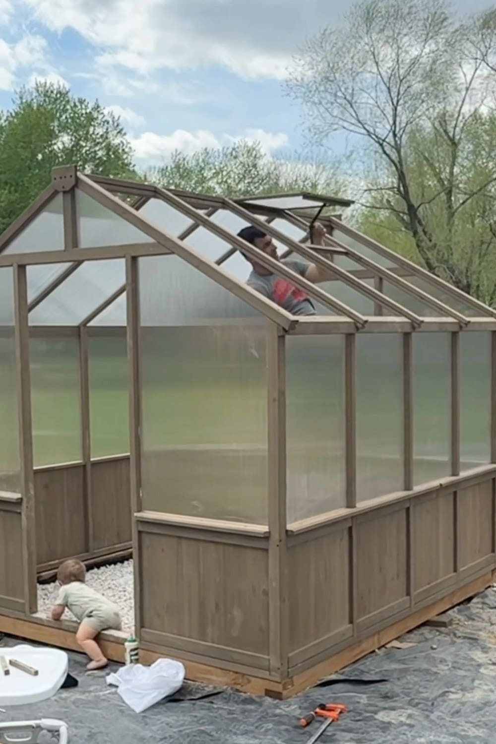 nstalling the roof vent on a backyard greenhouse near the end of assembly, with the polycarbonate panels, wood frame, and gravel base all in place.