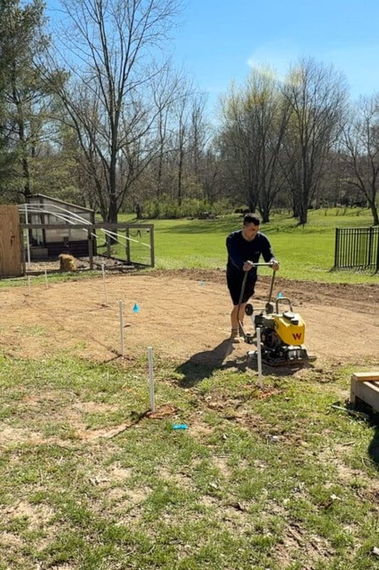 Using a plate compactor after adding soil to low areas to create a level base for garden beds