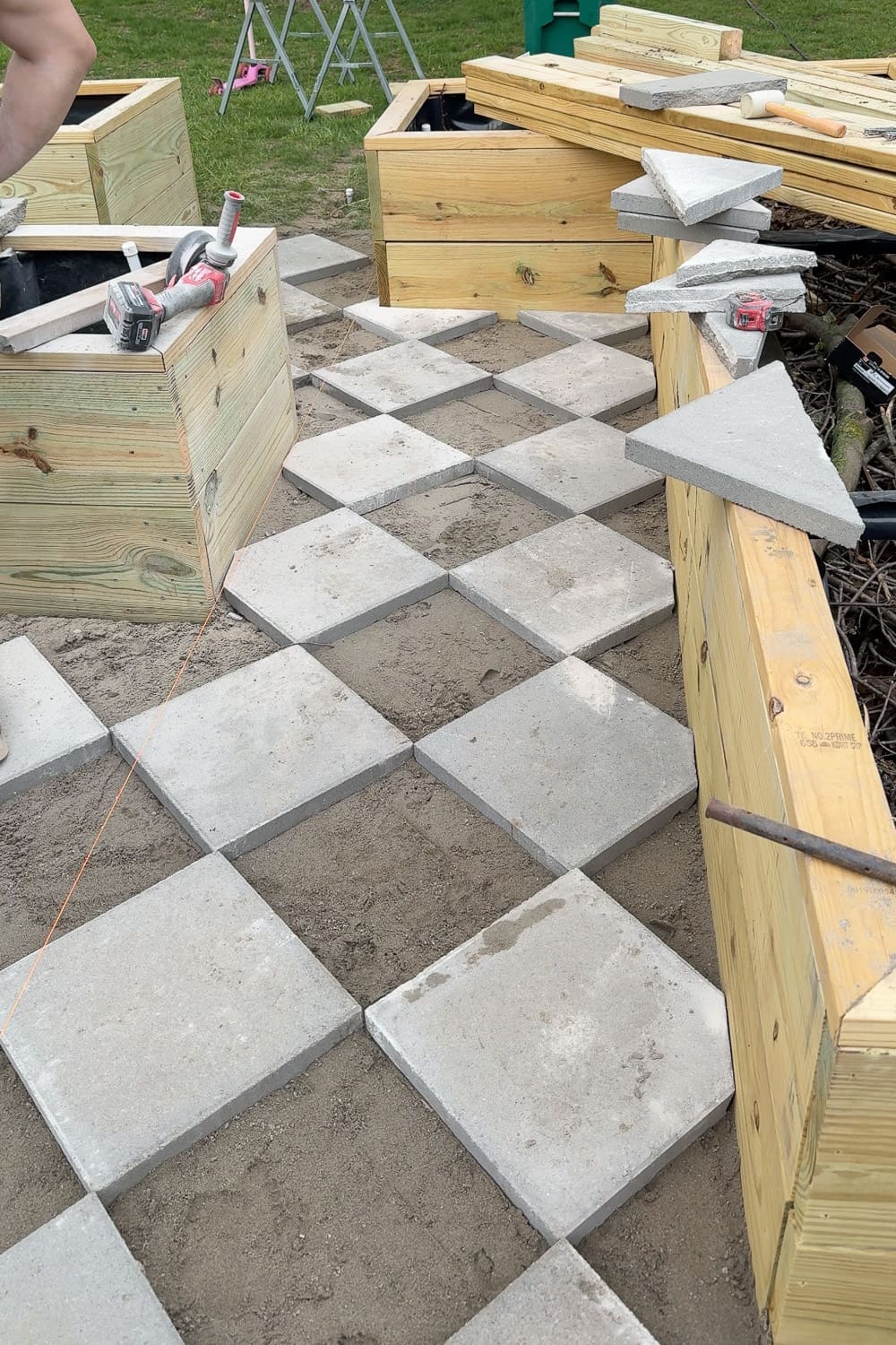 All square pavers laid out in a finished diamond checkerboard pattern between raised garden beds, ready for gravel to be added between each paver