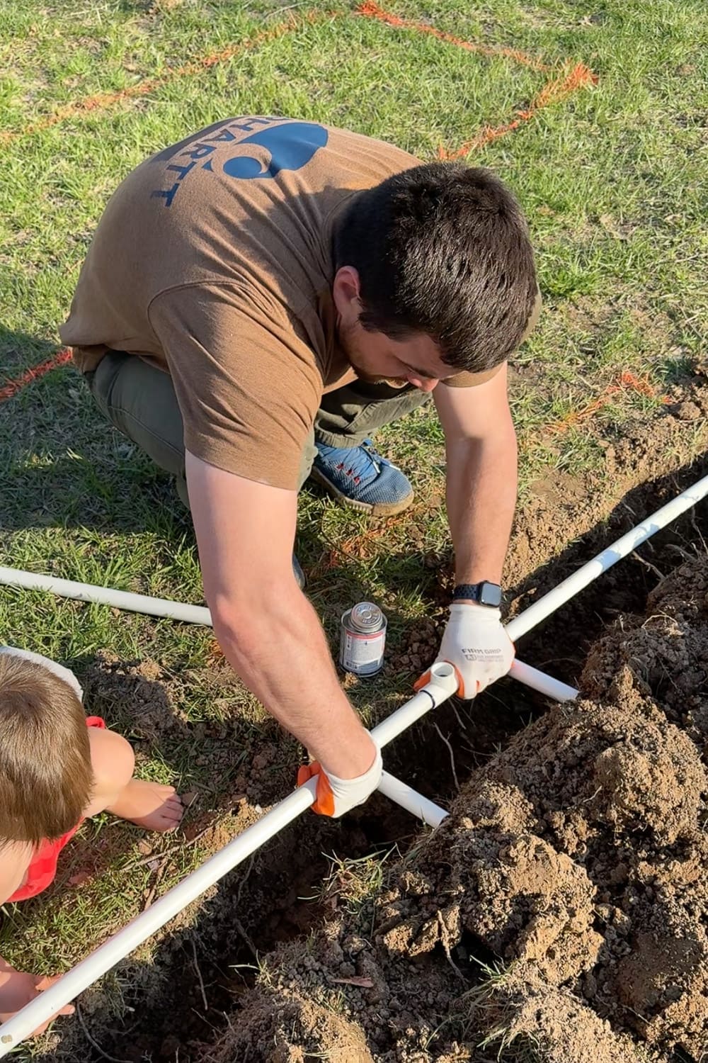 Pressing PVC pipe into a tee fitting after applying primer and cement to build a DIY garden watering system in the trench
