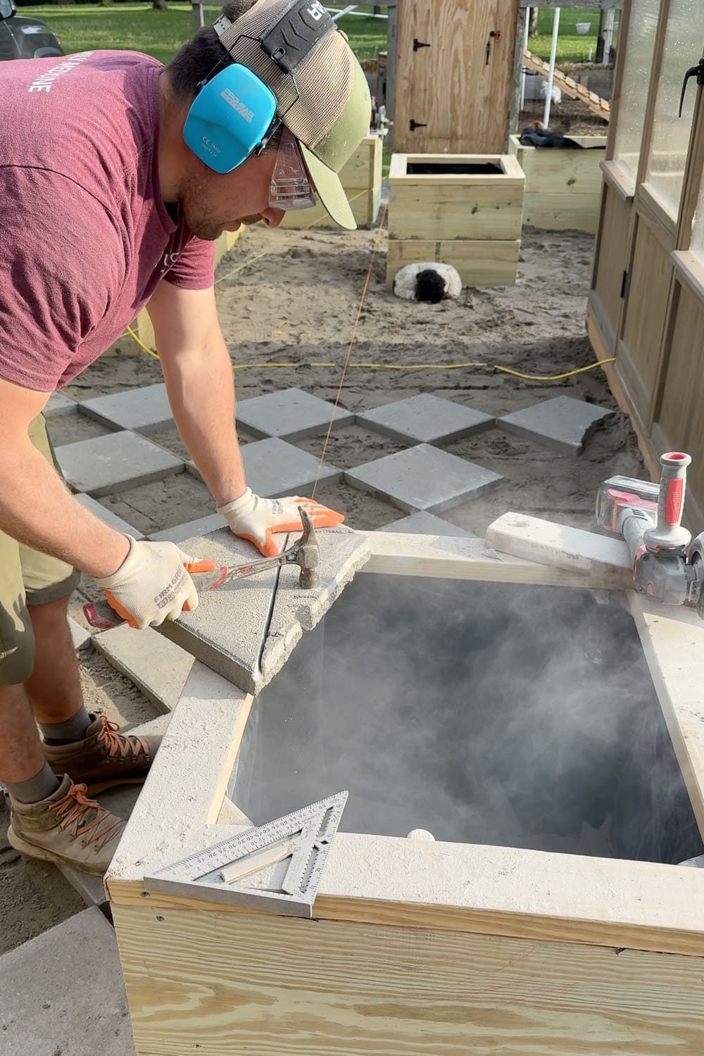 Using a hammer to break a scored concrete paver along a cut line to fit around the corner of a raised garden box