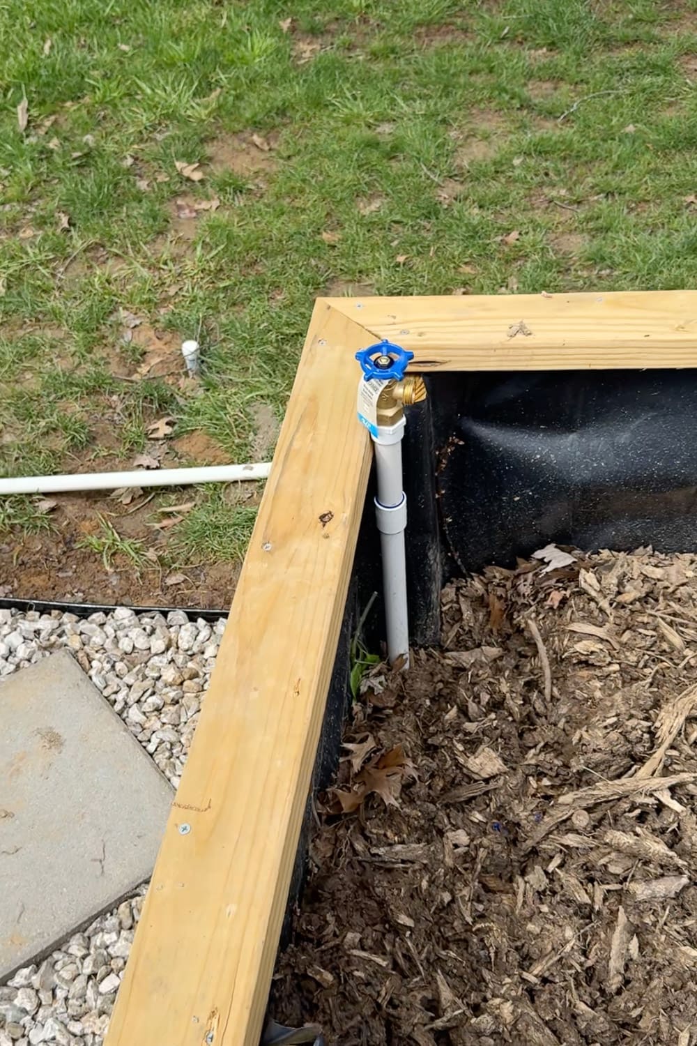 Close-up of a blue-handle spigot and PVC riser feeding a raised garden bed in a DIY irrigation system