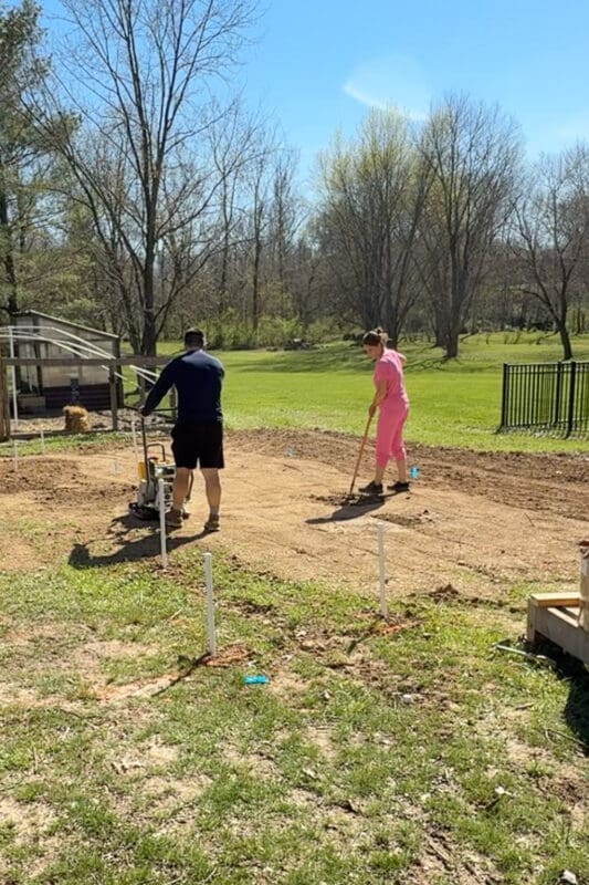 Adding and raking soil to fill low spots while leveling ground for garden beds before compacting