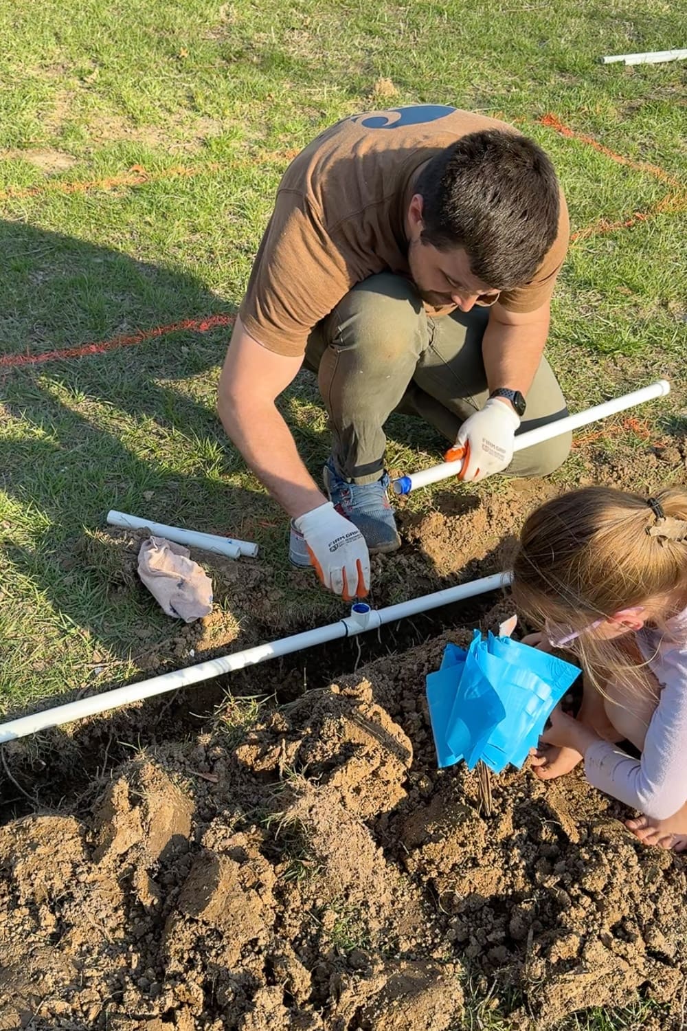 Applying PVC cement to a tee fitting in the trench to branch off the main line for a raised bed watering system spigot
