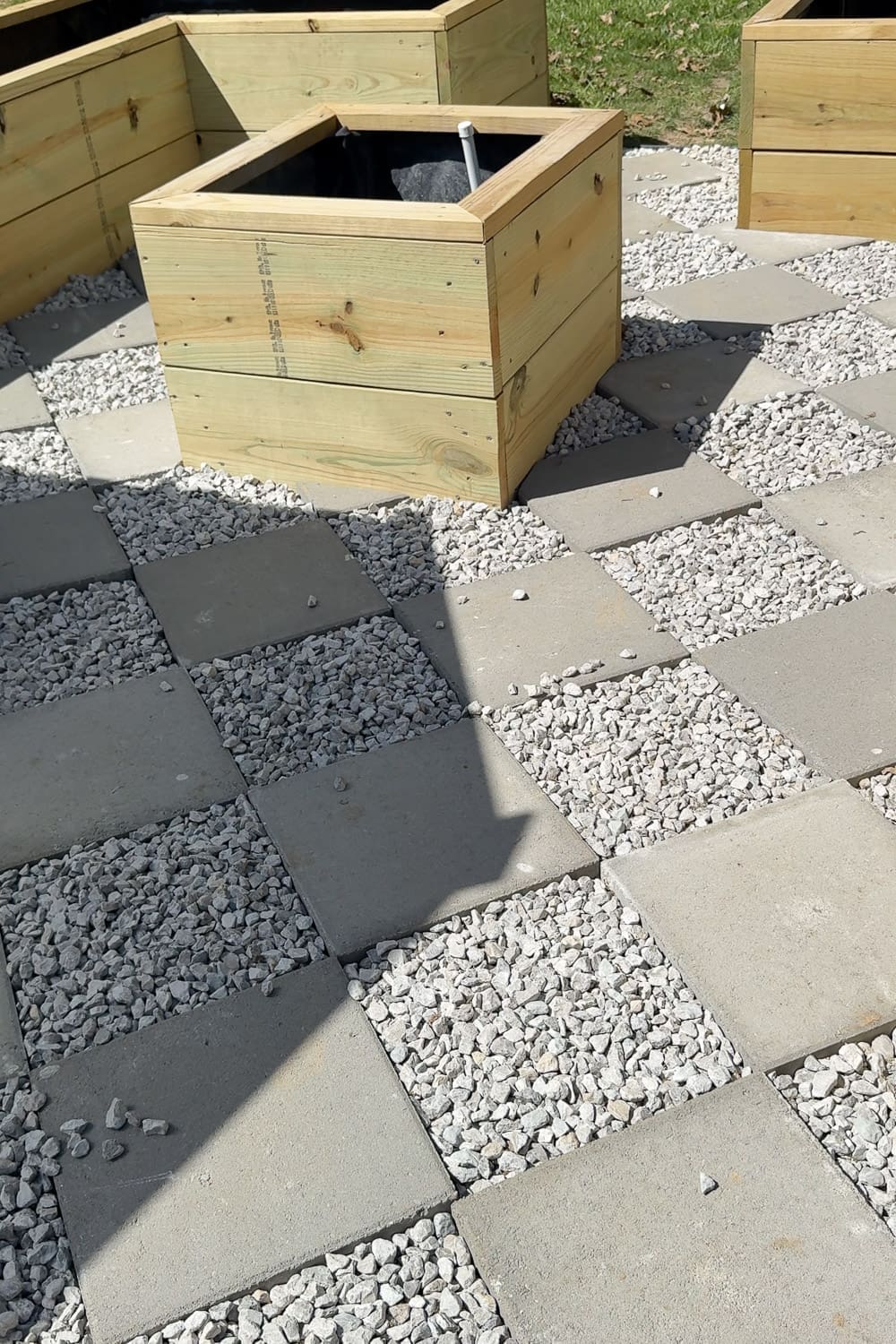 Gravel filling the gaps between square pavers in a diamond checkerboard pattern walkway, wrapping around the corner of a raised garden box