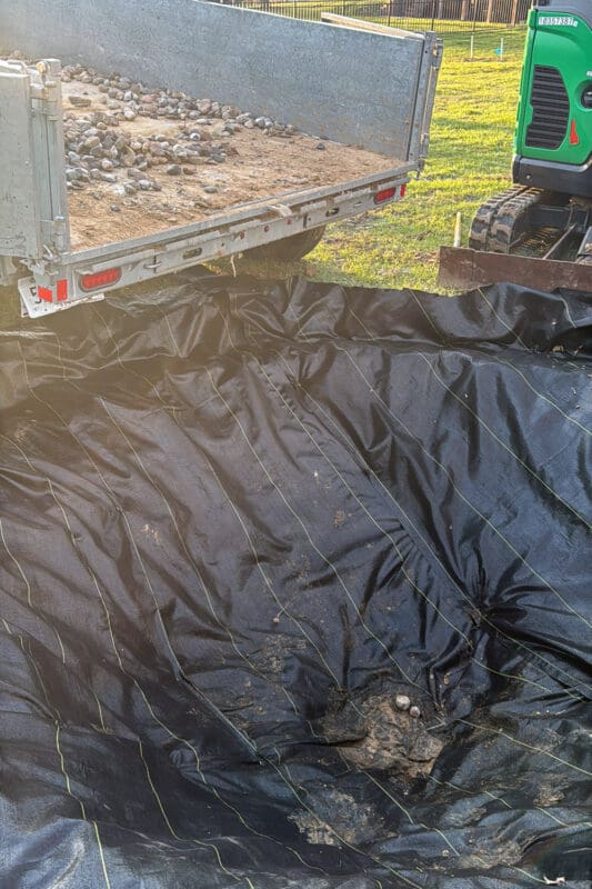Landscape fabric lining the bottom of a hole with rocks added for drainage