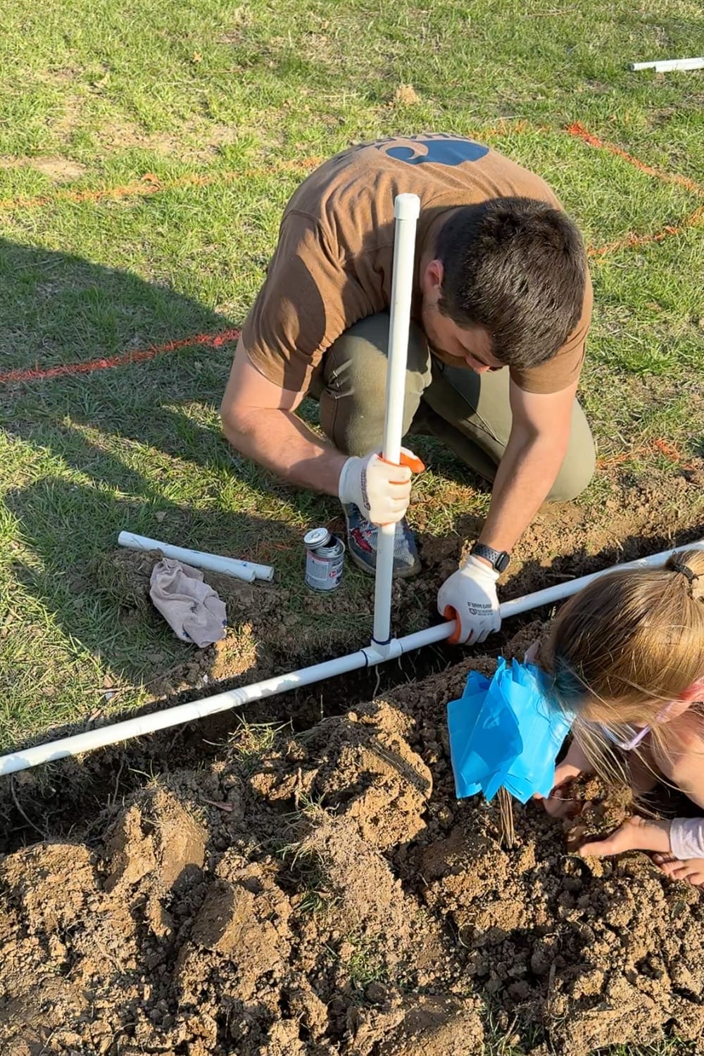 Inserting a vertical PVC spigot riser into a tee fitting along the buried main line of a DIY garden watering system