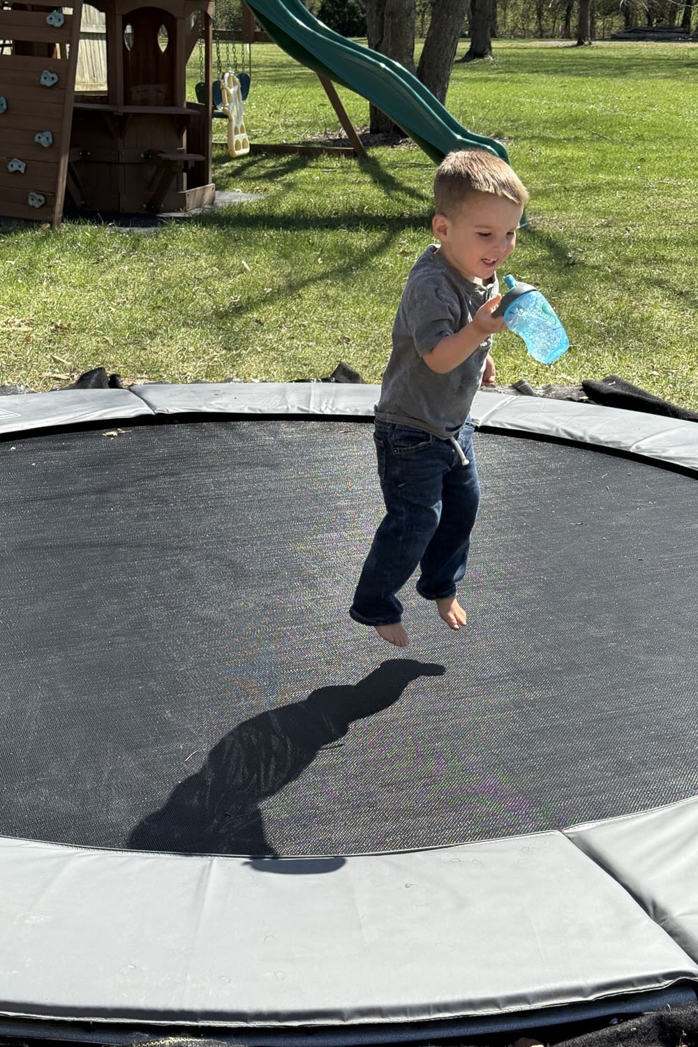 Child jumping on a finished in-ground trampoline in a backyard with a playset in the background