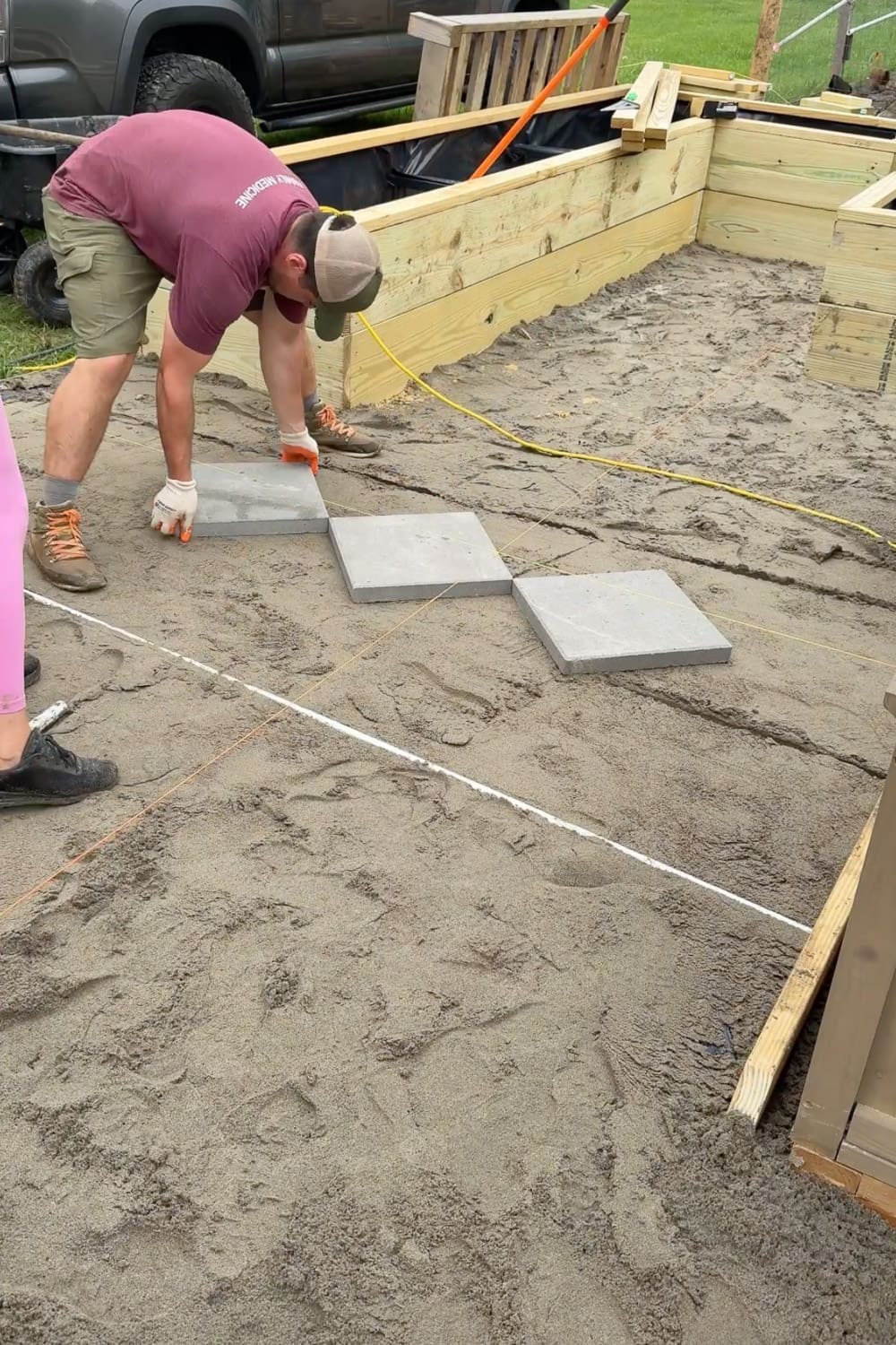 Laying square concrete pavers in a diamond checkerboard pattern on a leveled sand base, with evenly spaced gaps between each paver for gravel infill