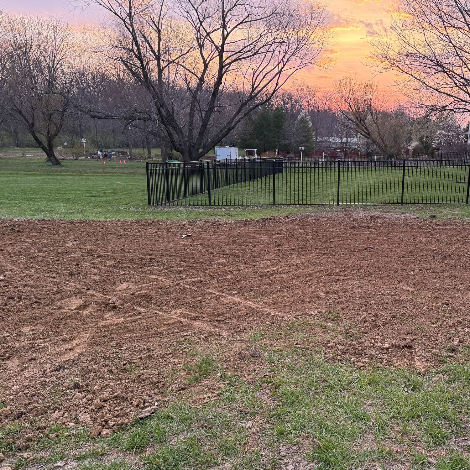 Flattened and leveled yard area prepared for raised garden beds with compacted dirt surface