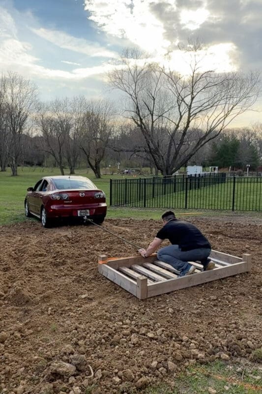 Creative DIY ground leveling technique using bed frame pulled by car to flatten soil for garden beds