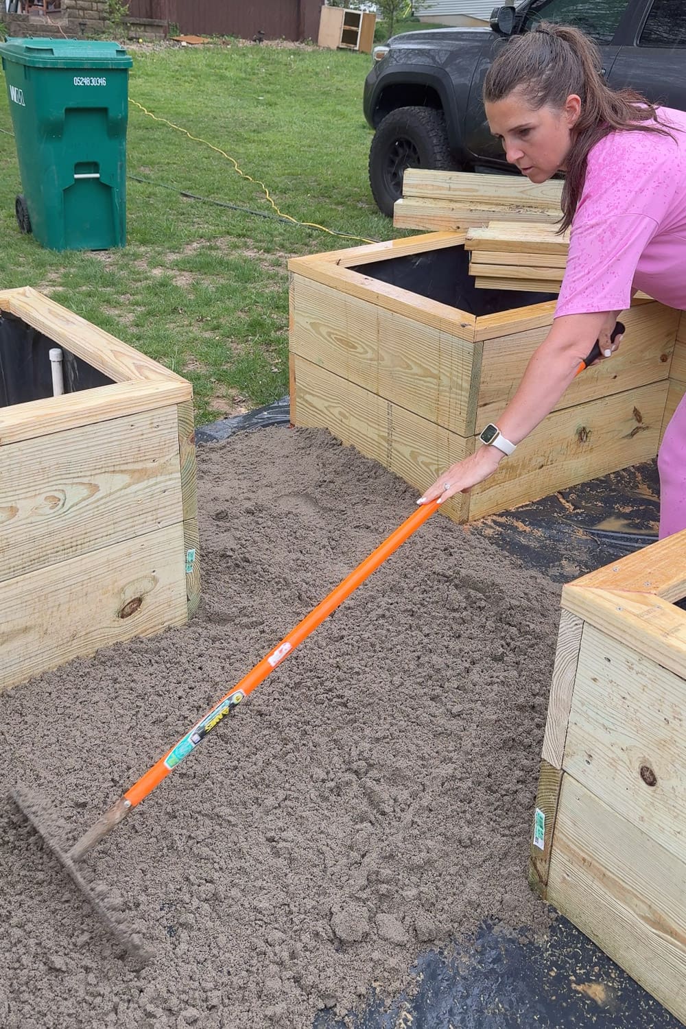 Raking and leveling sand to create a smooth, flat base for a DIY paver walkway between raised garden beds