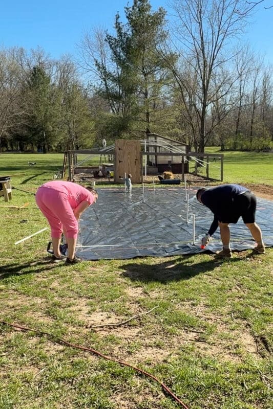 Measuring spacing and marking raised garden bed layout with spray paint on black weed barrier