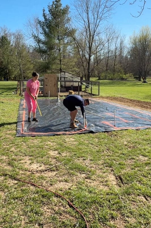 Measuring and marking raised garden bed layout with spray paint on top of black weed barrier