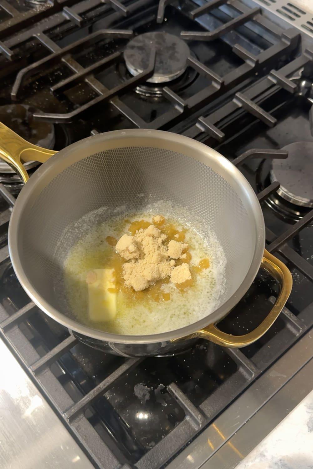 Butter and brown sugar melting together in a small stainless steel saucepan with gold handles on a gas stovetop, the first step in making the cinnamon swirl filling for cinnamon roll pancakes.