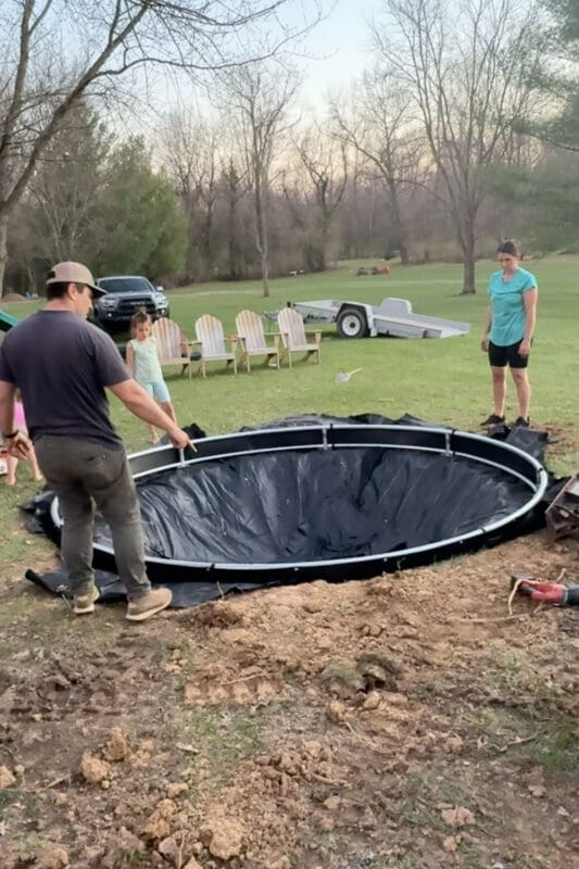 Setting the trampoline frame into an in-ground trampoline hole lined with landscape fabric in a backyard
