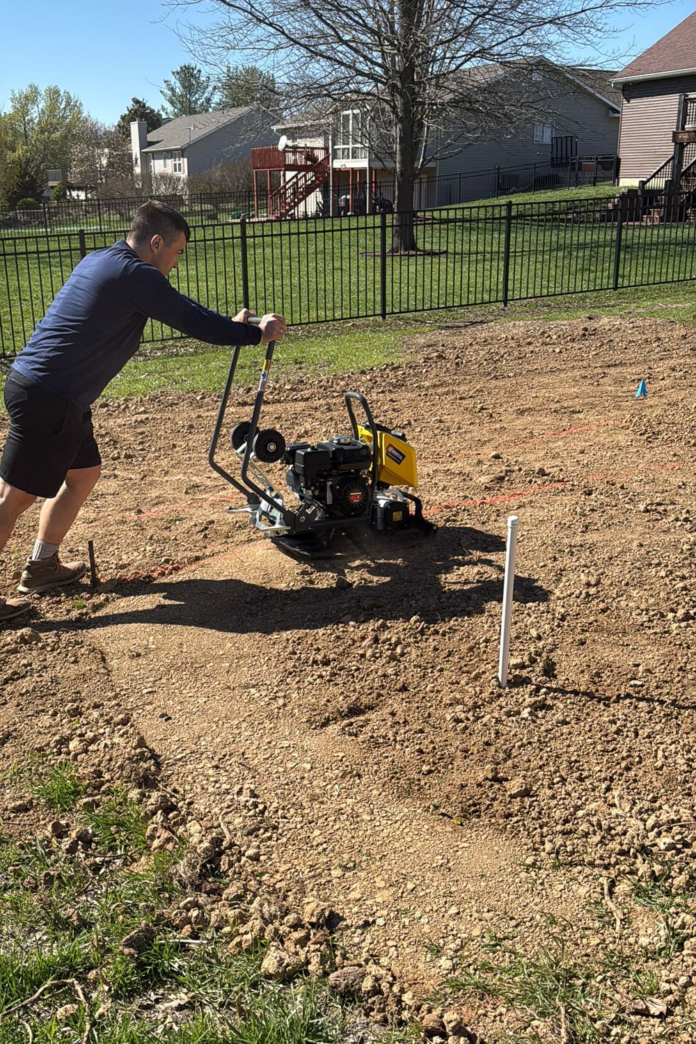 Using a plate compactor to compact and level soil for garden beds after spreading and grading dirt