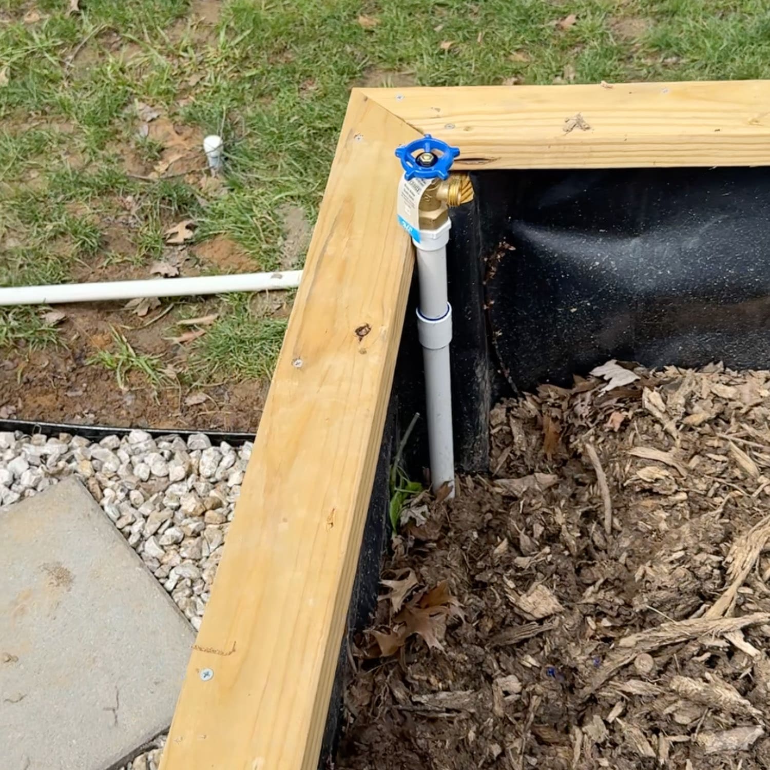 PVC pipe spigot installed at the corner of a wooden raised garden bed for a DIY watering system