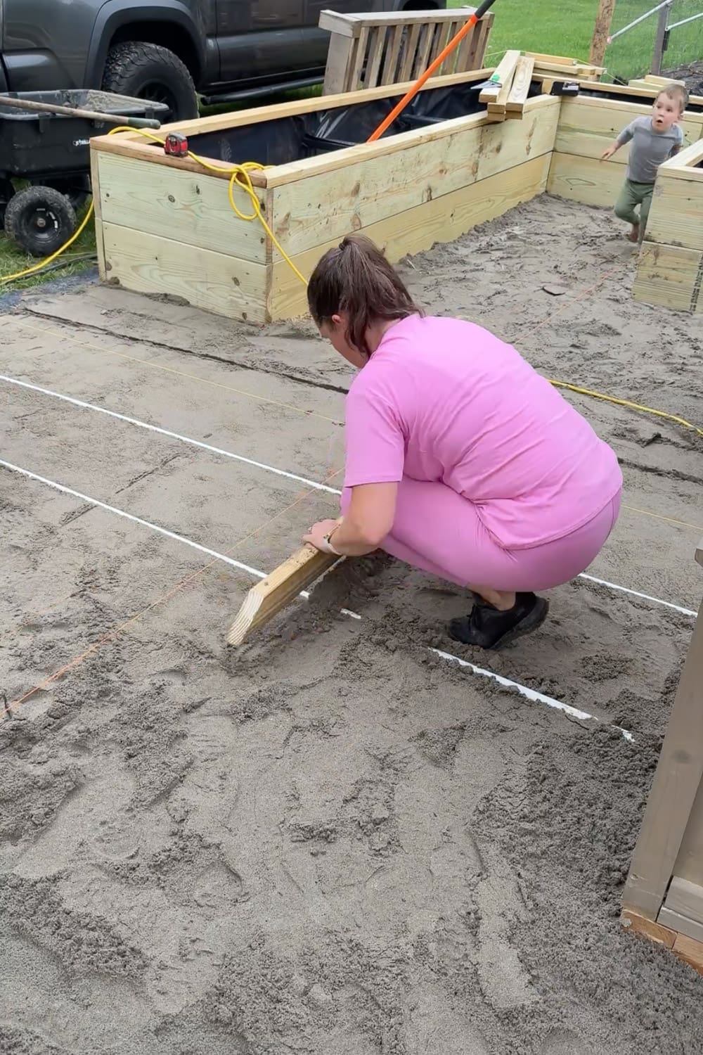 Screeding a wooden board along a string line to create a flat, level sand base for a diamond pattern paver walkway