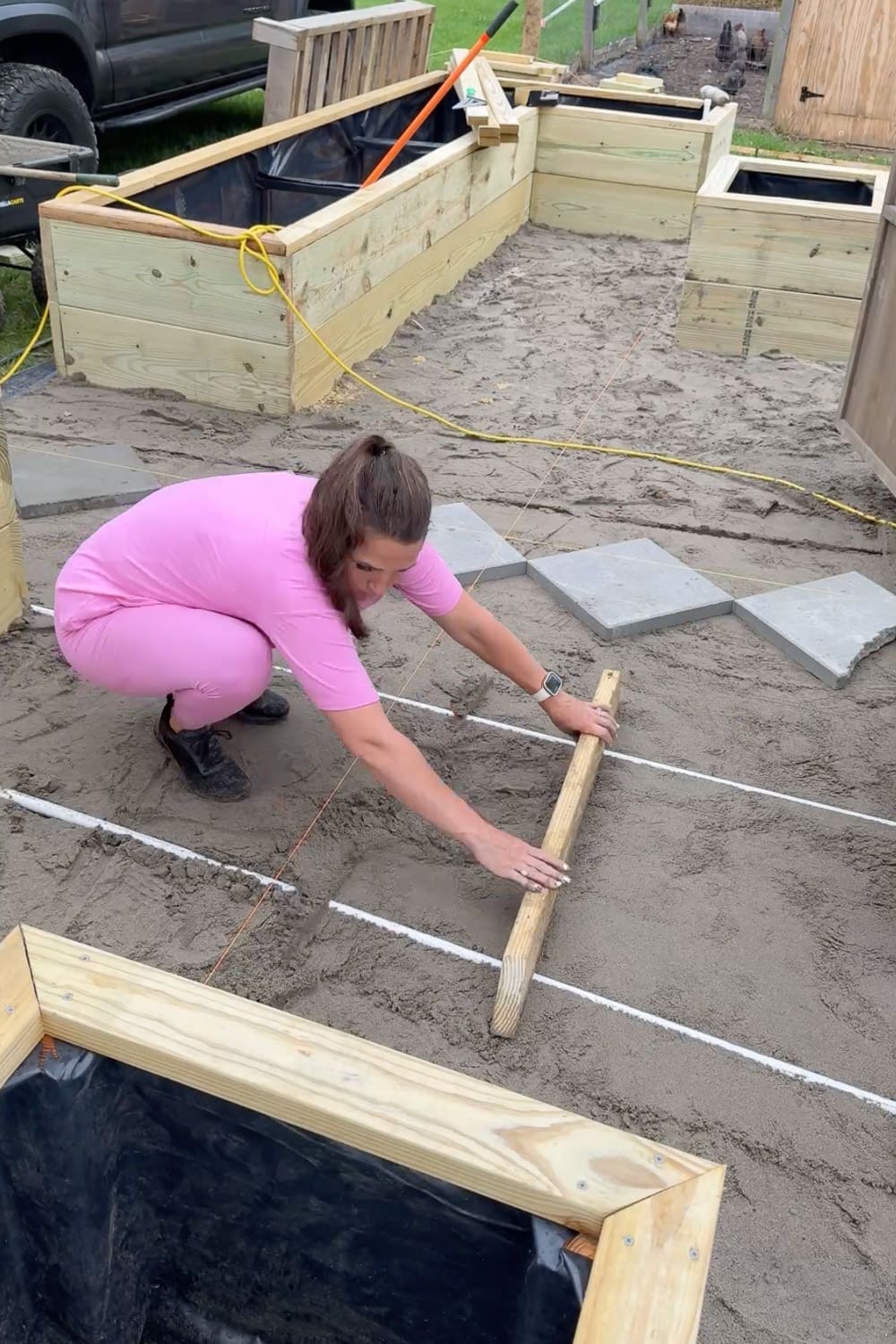 Smoothing and leveling the sand base with a wooden board along the string grid before laying pavers, with the first pavers already in place