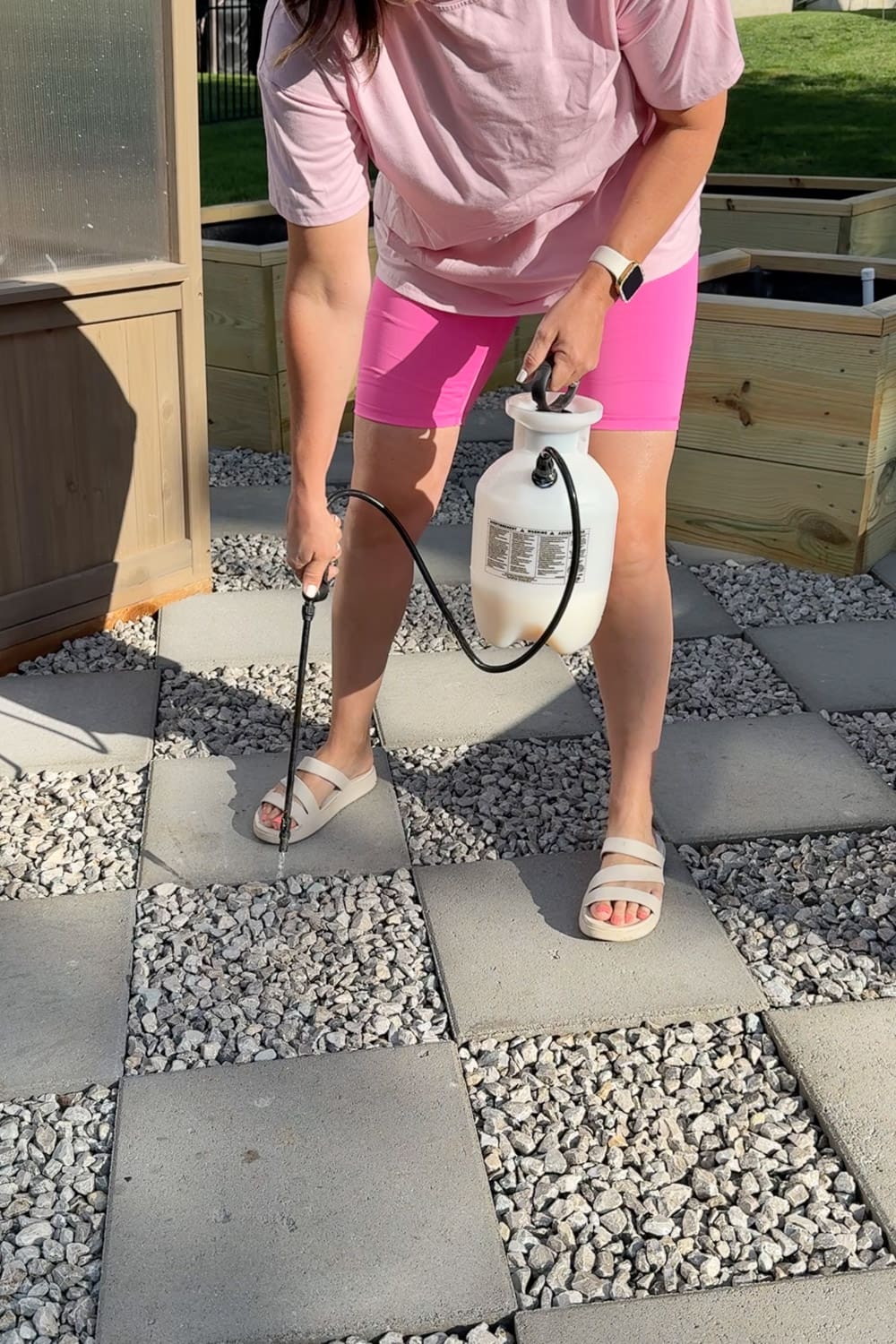 Applying mulch glue with a pump sprayer to lock the gravel in place between square pavers on a finished DIY paver walkway