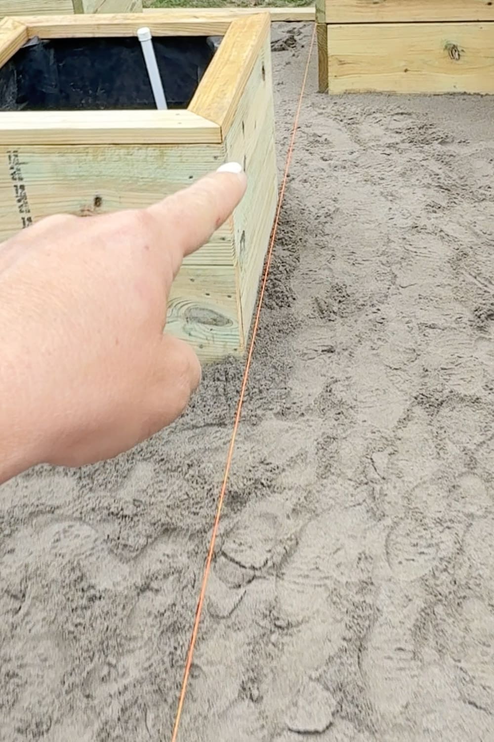 Using a string line along a raised garden bed to mark a straight edge for laying pavers in a diamond pattern