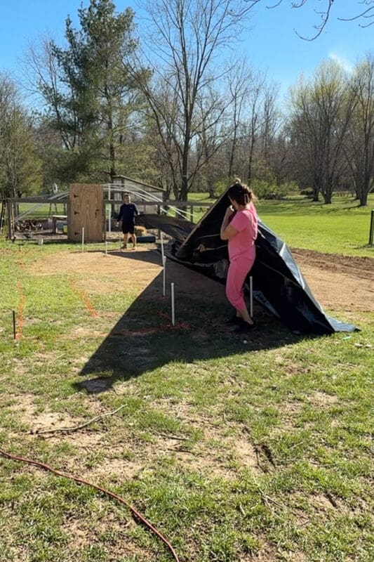 Unfolding black plastic weed barrier to cover large garden area before installing raised beds to control weeds in the garden.