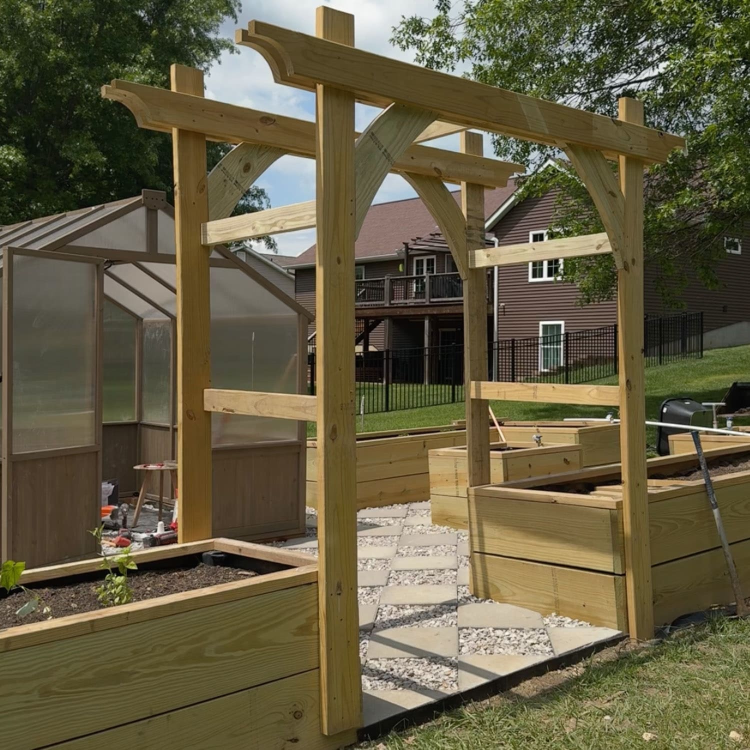 Side angle view of a wooden DIY garden trellis arbor with horizontal cross supports for climbing plants, positioned at the entrance of a backyard vegetable garden with raised planter boxes