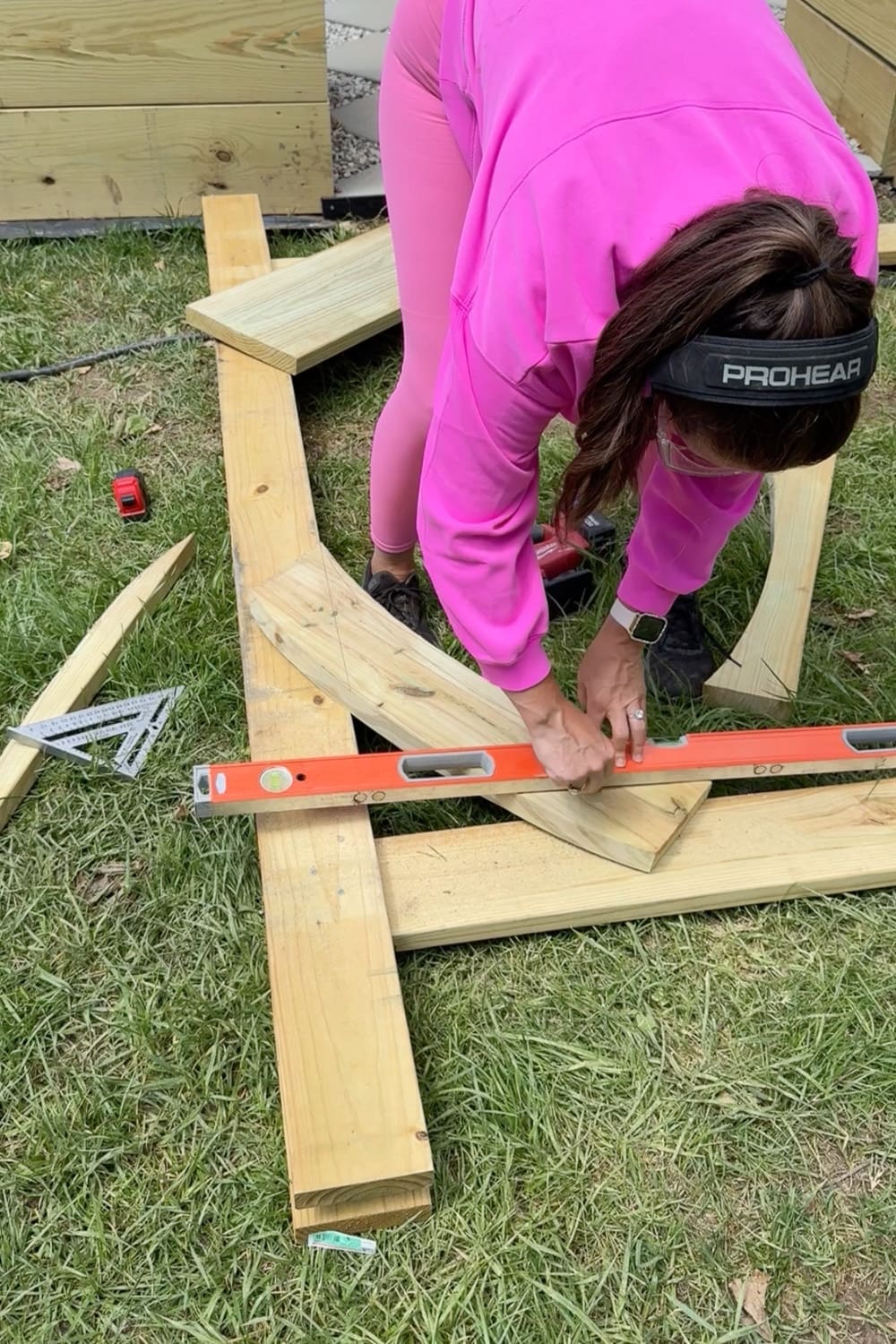 Woman in pink using an orange level to check that the wooden frame pieces of a DIY garden trellis arbor are properly aligned before final assembly