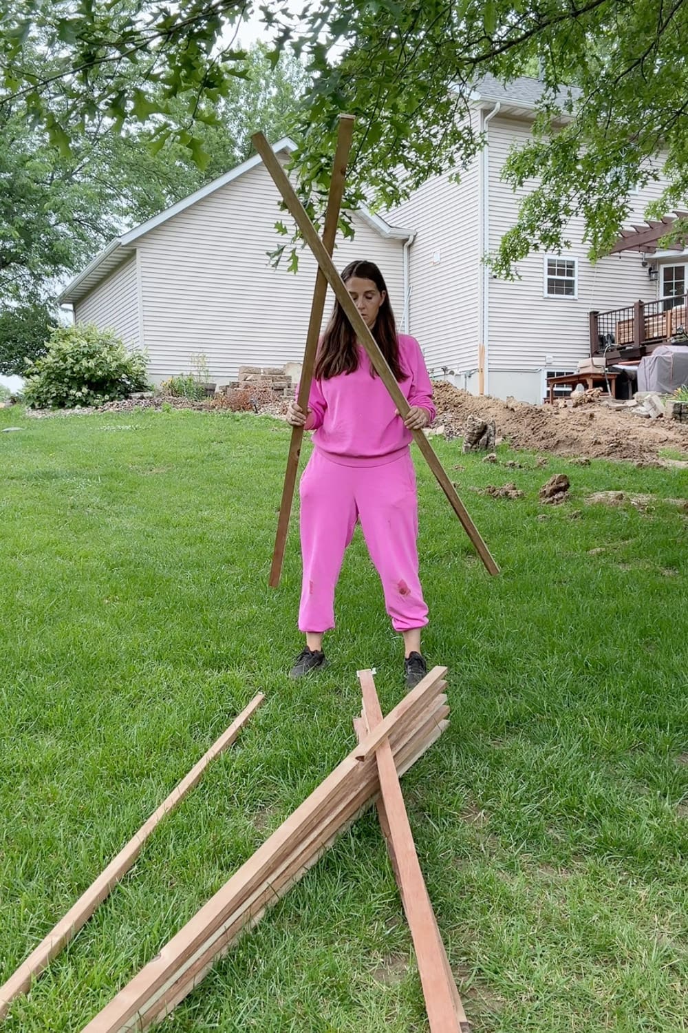 Gardener holding up an assembled X-shaped wood frame for a wood garden climbing support, with extra stakes laid out on the grass