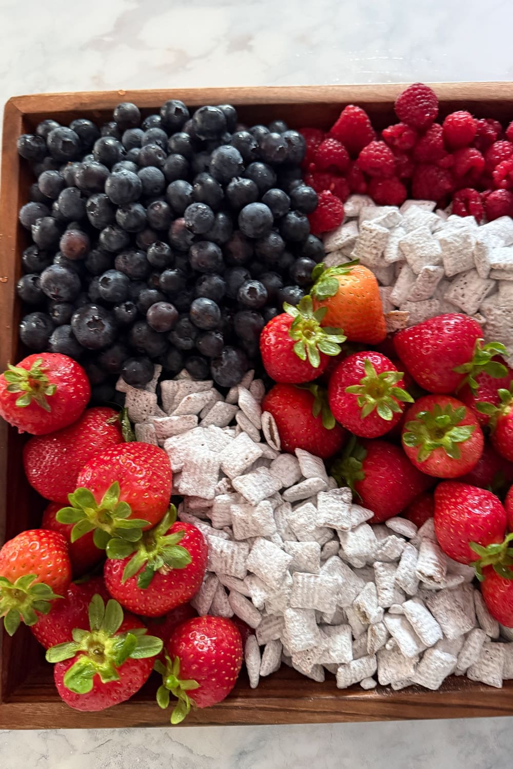 Easy patriotic fruit tray featuring fresh berries and puppy chow in a wooden tray