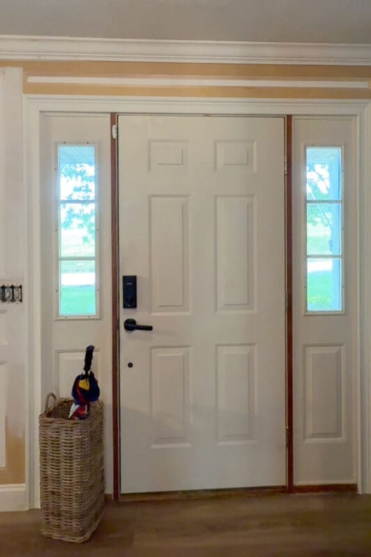 Empty entryway before decorating, showing white front door with sidelights and a wicker umbrella basket