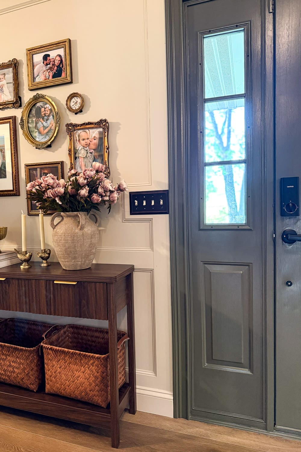 Entryway decor featuring a painted green front door beside a gold-framed gallery wall and styled console table with peonies