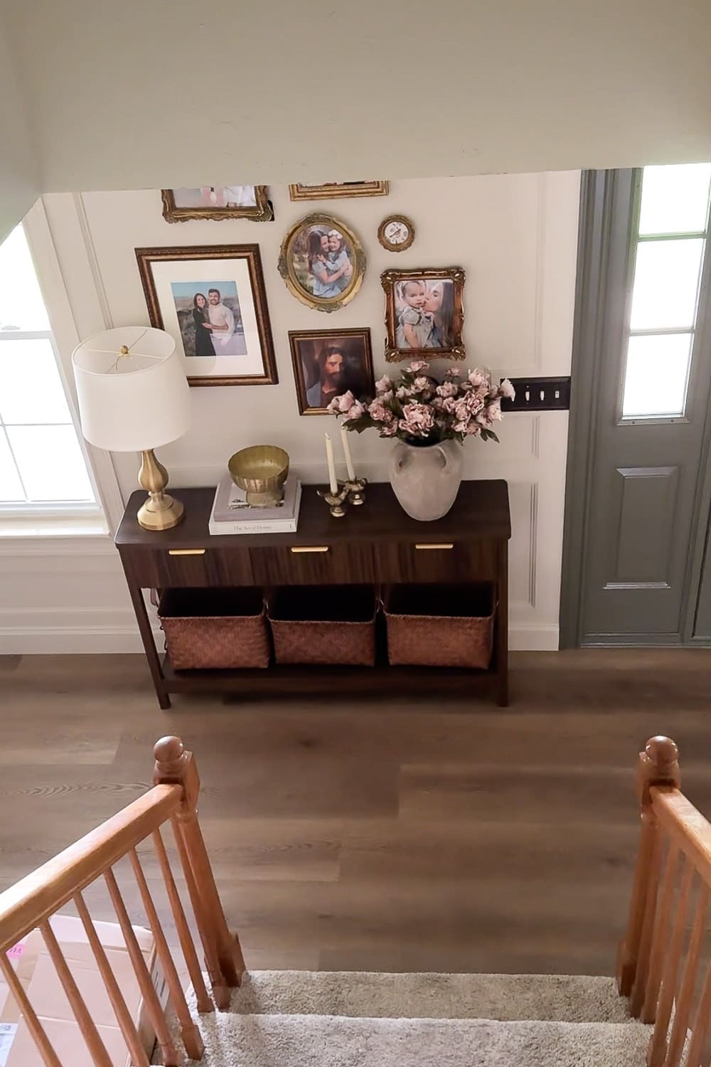 Entryway decor viewed from the staircase, featuring a styled console table, gold gallery wall, woven baskets, and blue front door