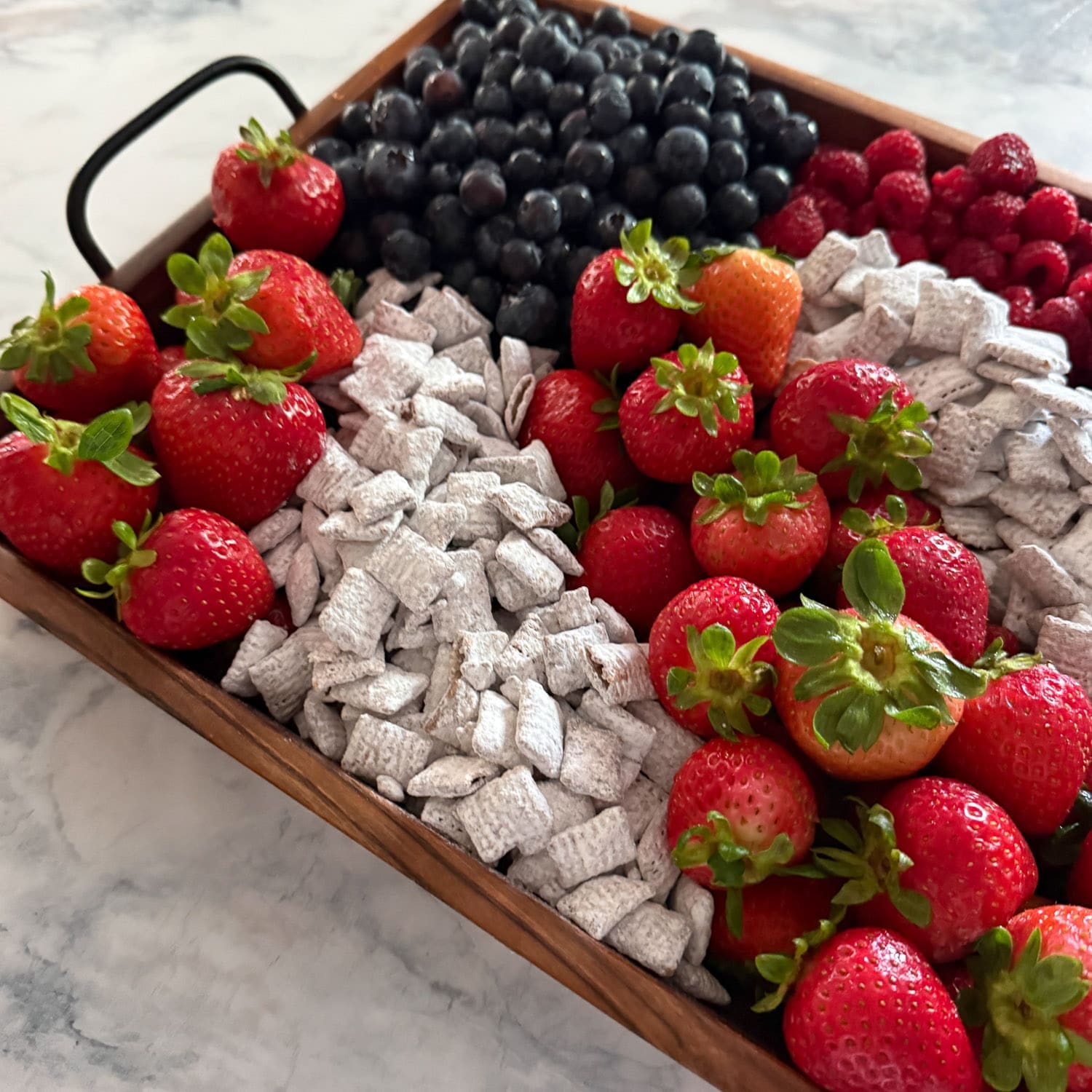 Patriotic fruit tray in a wooden serving tray with handles, filled with red, white, and blue ingredients for the 4th of July