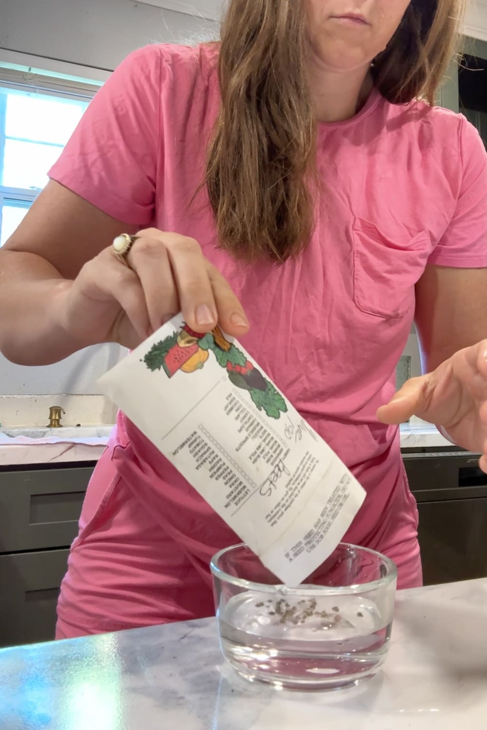 Woman pouring beet seeds from a seed packet into a bowl of water to soak before planting in a raised bed garden