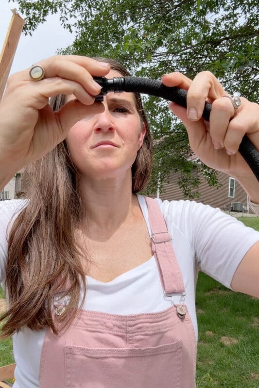 Crystel attaching a black end cap fitting onto the end of a soaker hose in her backyard garden