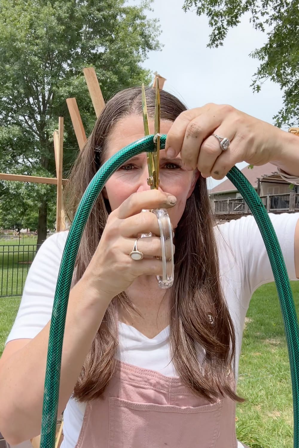 Crystel using scissors to cut a green garden hose to length for customizing the length in a garden watering system.