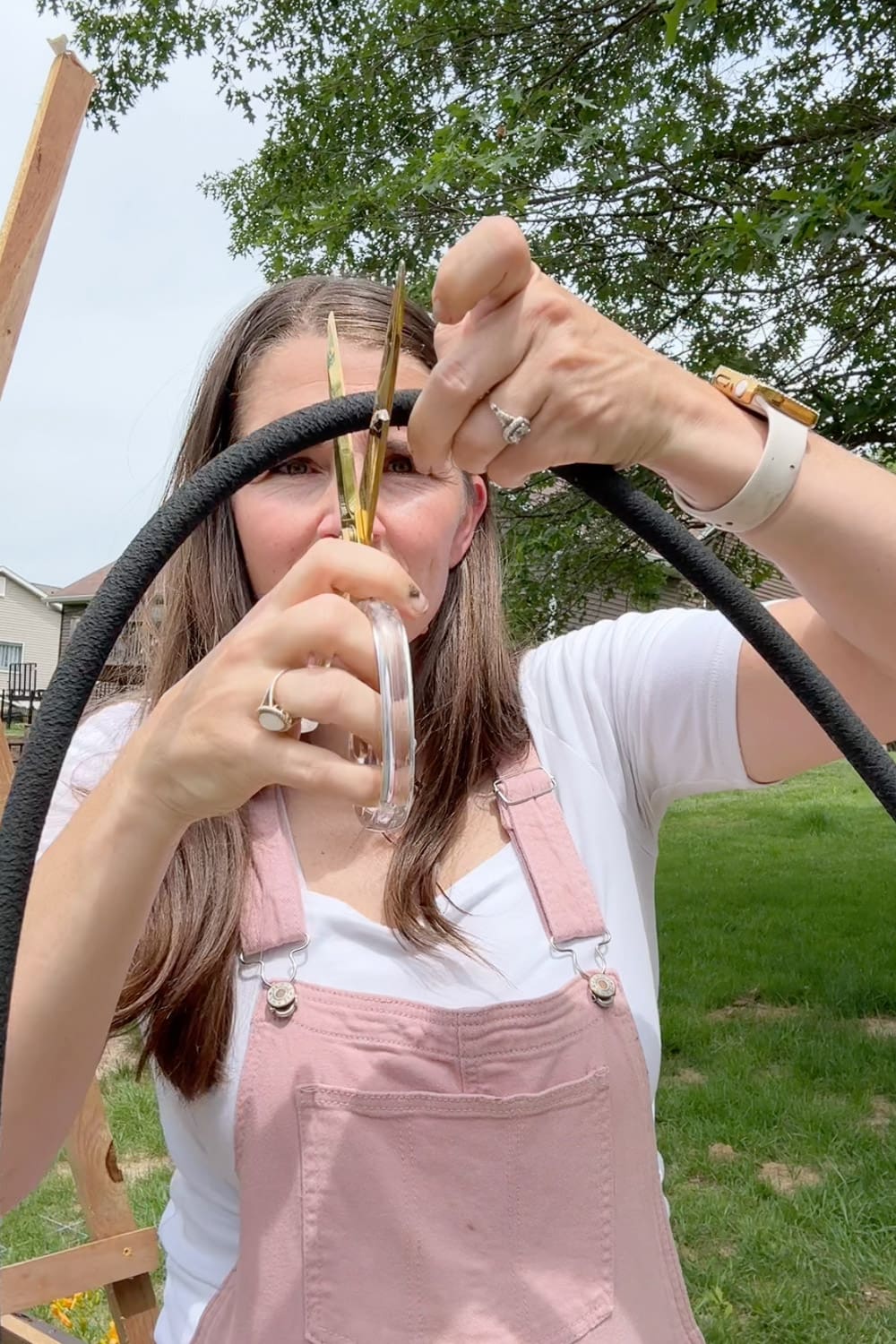 Crystel using scissors to cut a black soaker hose to length for installing in her raised garden beds